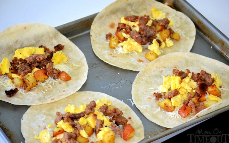 four breakfast burritos being made on baking sheet