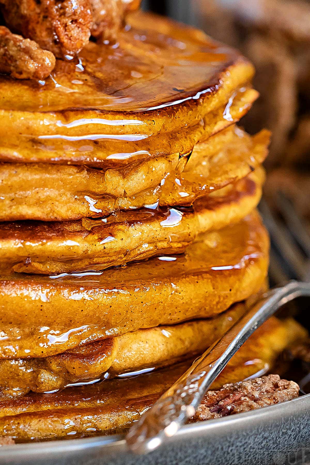 close up of a stack of pumpkin pancakes with maple syrup and candied pecans on top
