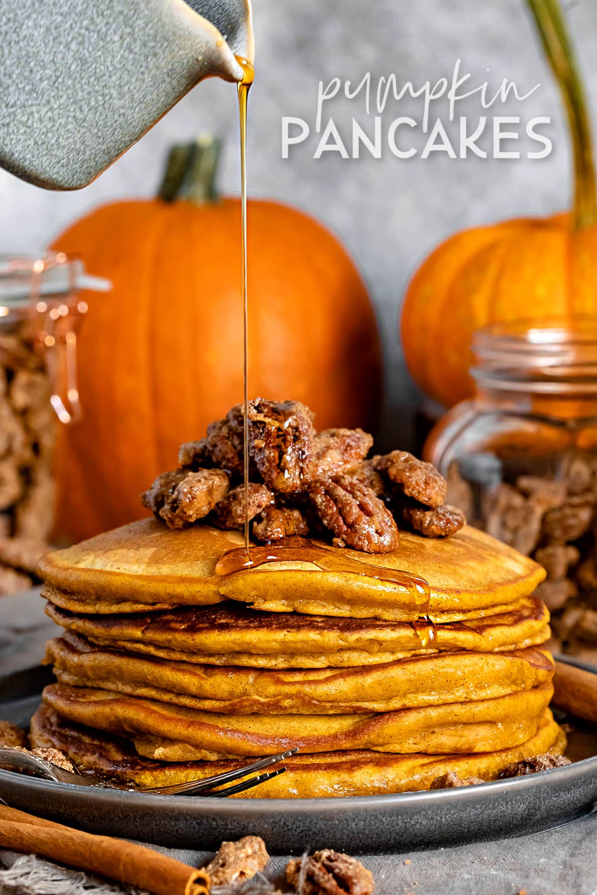 stack of pumpkin pancakes with candied pecans on top and syrup being drizzled onto pancakes