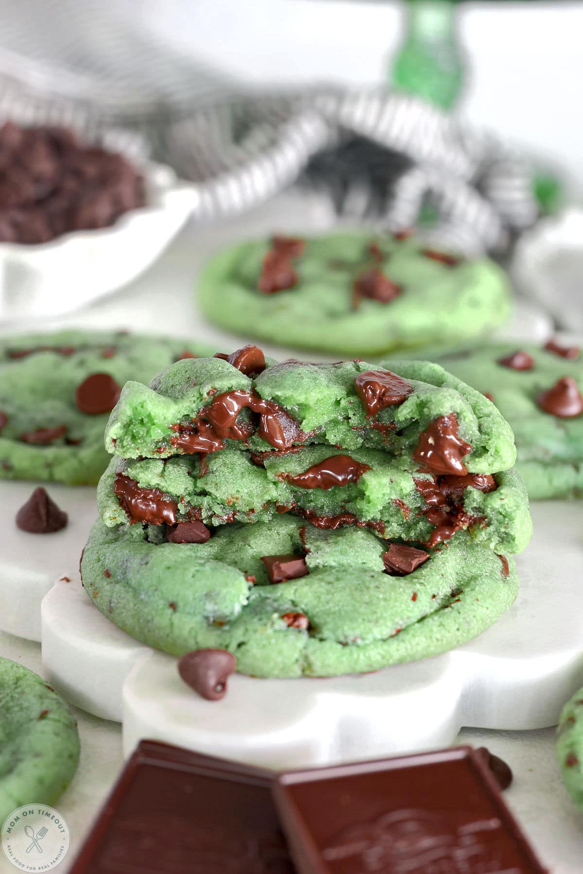 Stack of mint chocolate chip cookies on scalloped white marble board. Top cookie is cut in half.