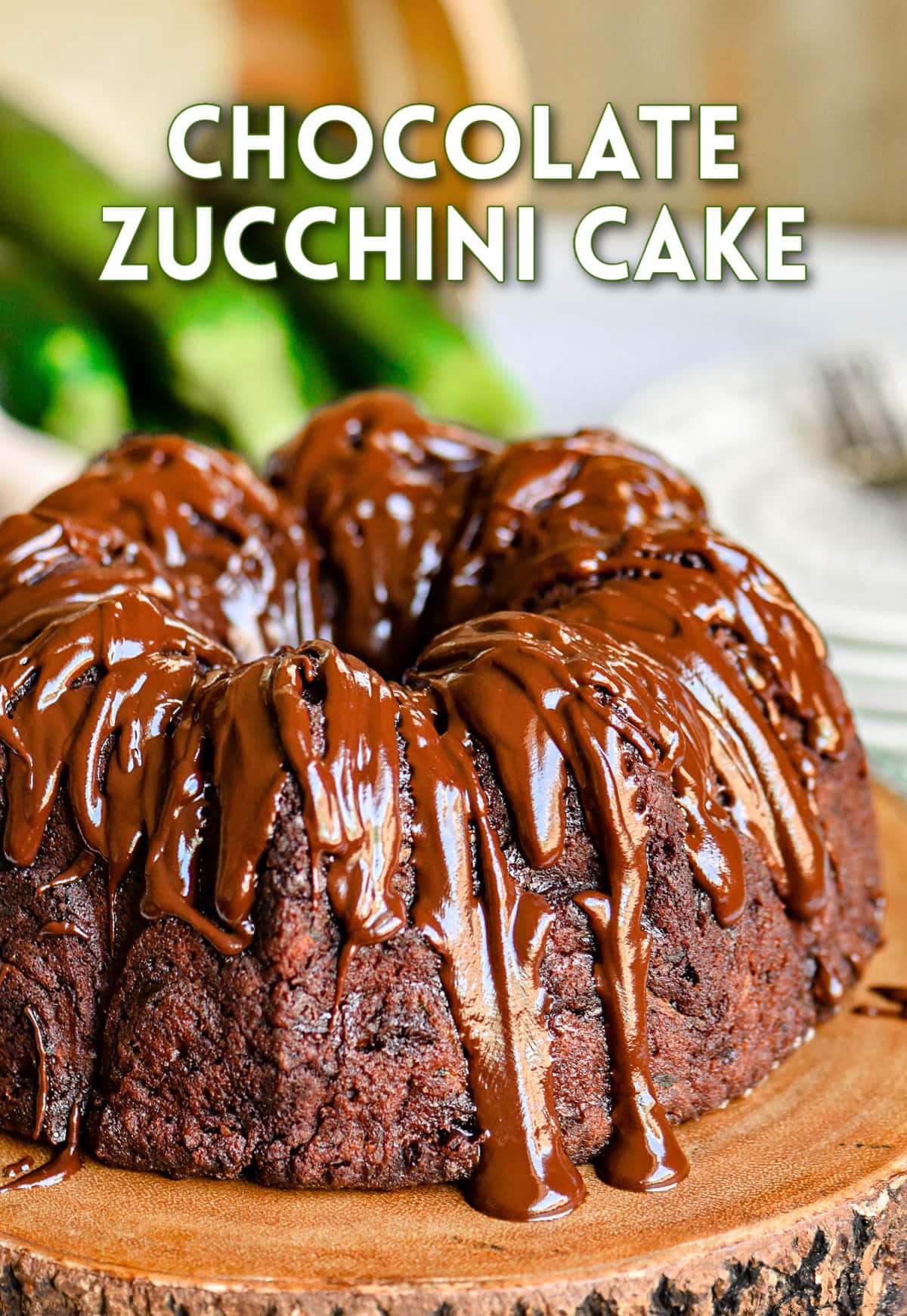 whole chocolate zucchini bundt cake on wood cake stand with rich chocolate glaze on top of cake.