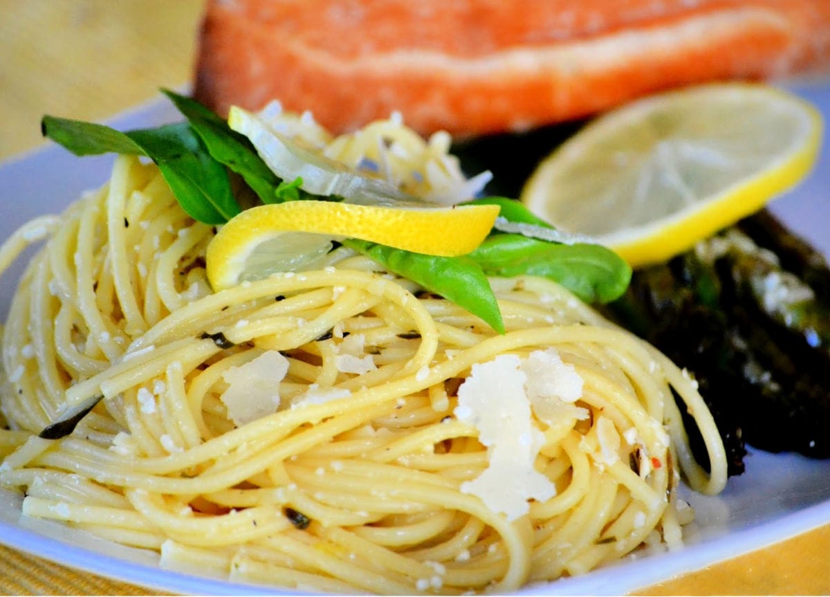 lemon spaghetti on white plate with asparagus and salmon garnished with lemon and basil and Parmesan