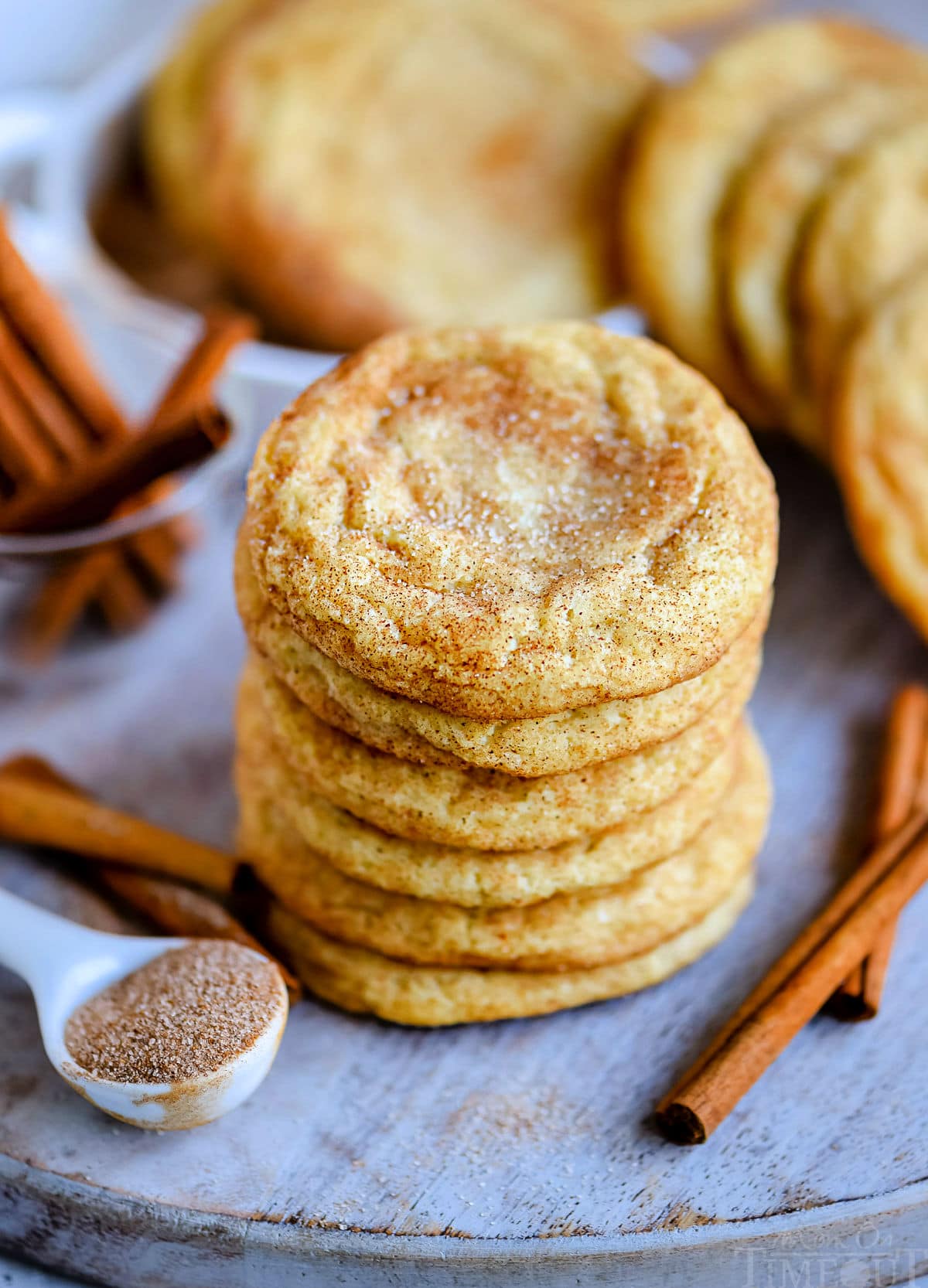 6 snickerdoodle cookies stacked on blue board with cinnamon sticks on the side