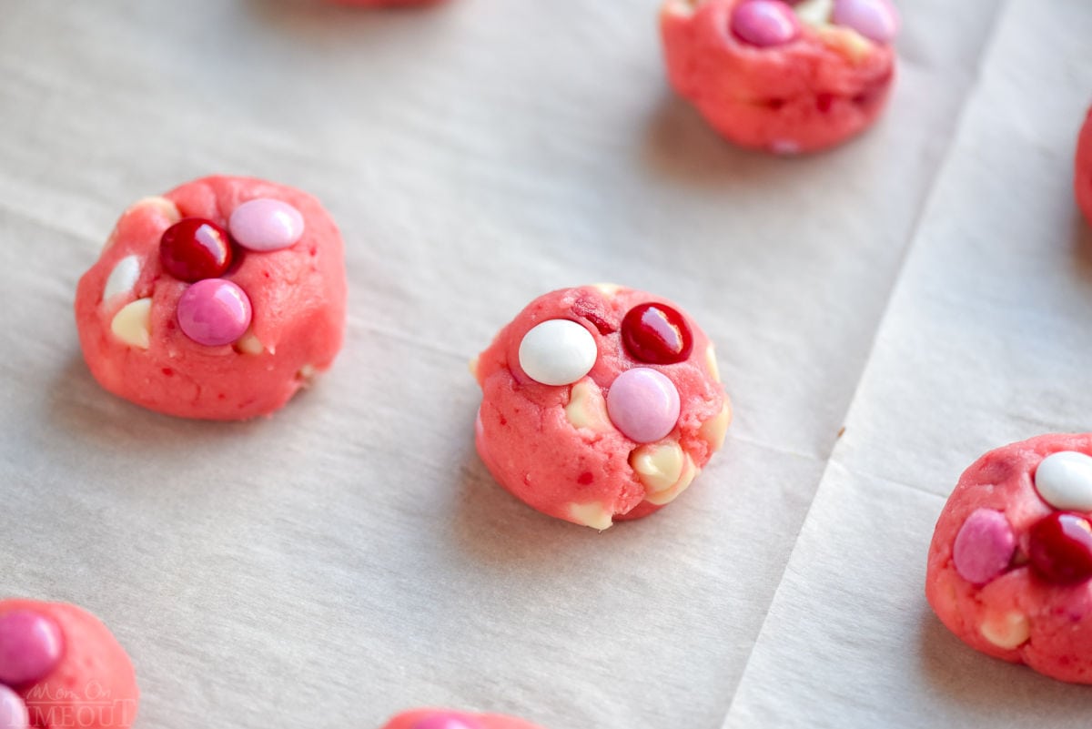 cookie dough balls topped with m&ms on a parchment lined cookie sheet ready to be baked.