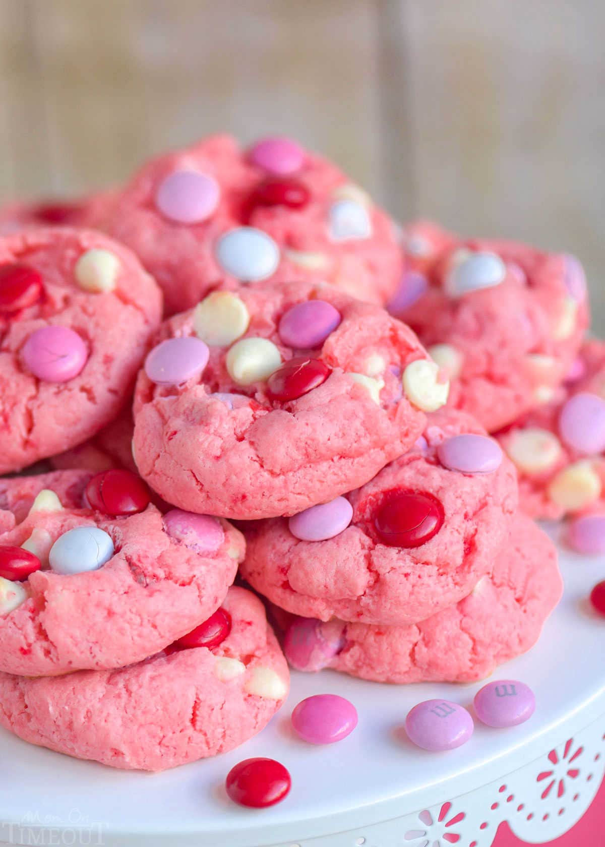 strawberry cake mix cookies made with M and Ms and white chocolate chips piled high on a white metal cake stand.