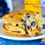 a stack of Blueberry Buttermilk Pancakes on white plate with syrup on a blue placemat