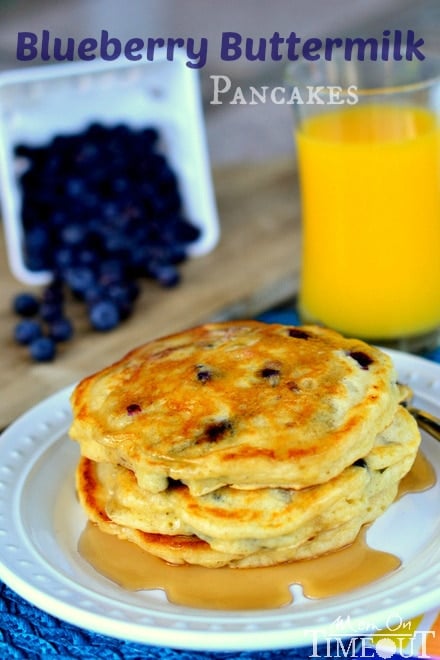  a stack of Blueberry Buttermilk Pancakes on white plate with syrup on a blue placemat and fresh blueberries in the background