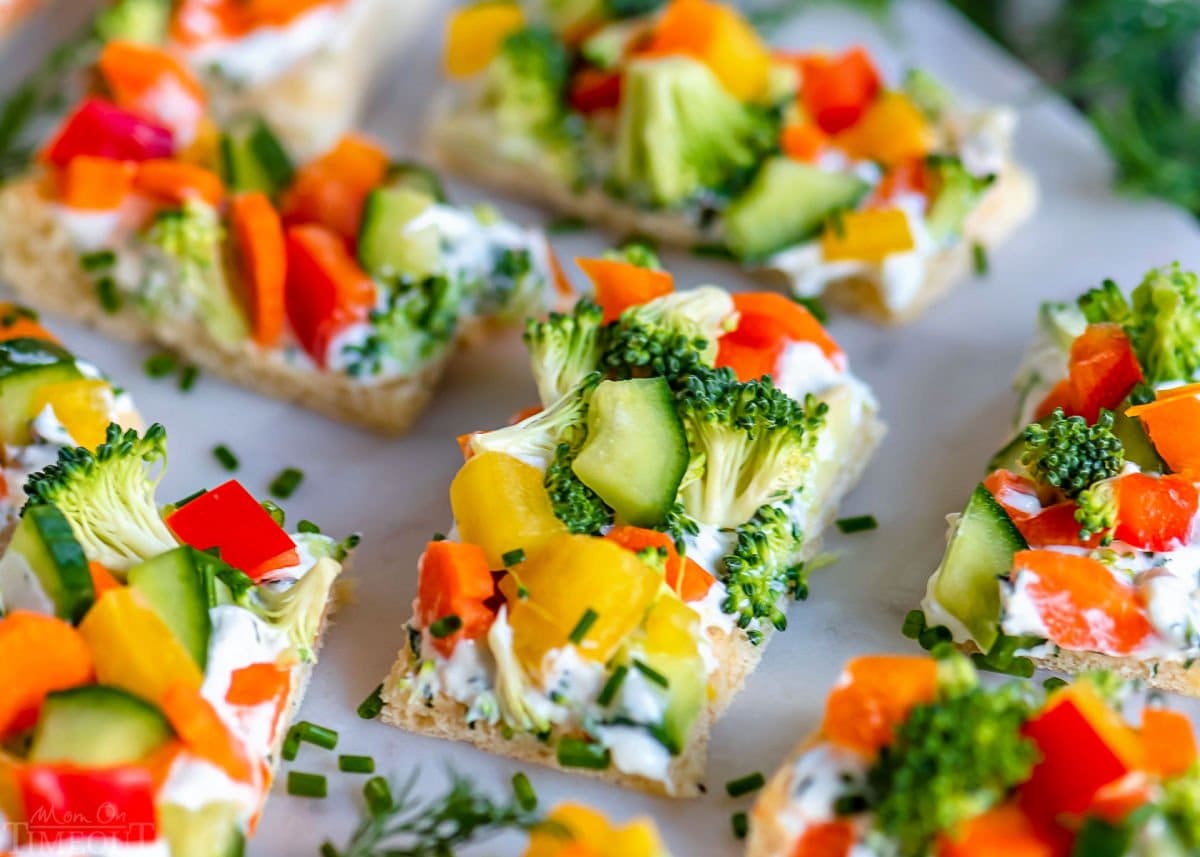 close up look at veggie pizza cut into small rectangles and placed on marble serving board.