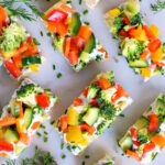 veggie pizza party appetizer cut into rectangles and sprinkled with fresh herbs. sitting on white marble.