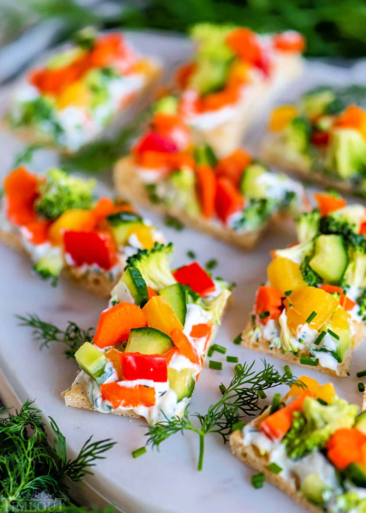veggie pizza cut into rectangles sitting on marble board garnished with fresh sprigs of dill.