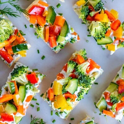 top down view of veggie pizza recipe assemble and cut into small pieces for serving. dill sprigs are scattered about on the marble cutting board.