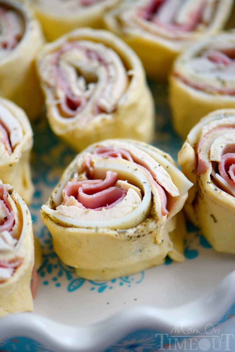 rolled up crescent rolls with ham chicken and cheese in white pie dish ready to be baked