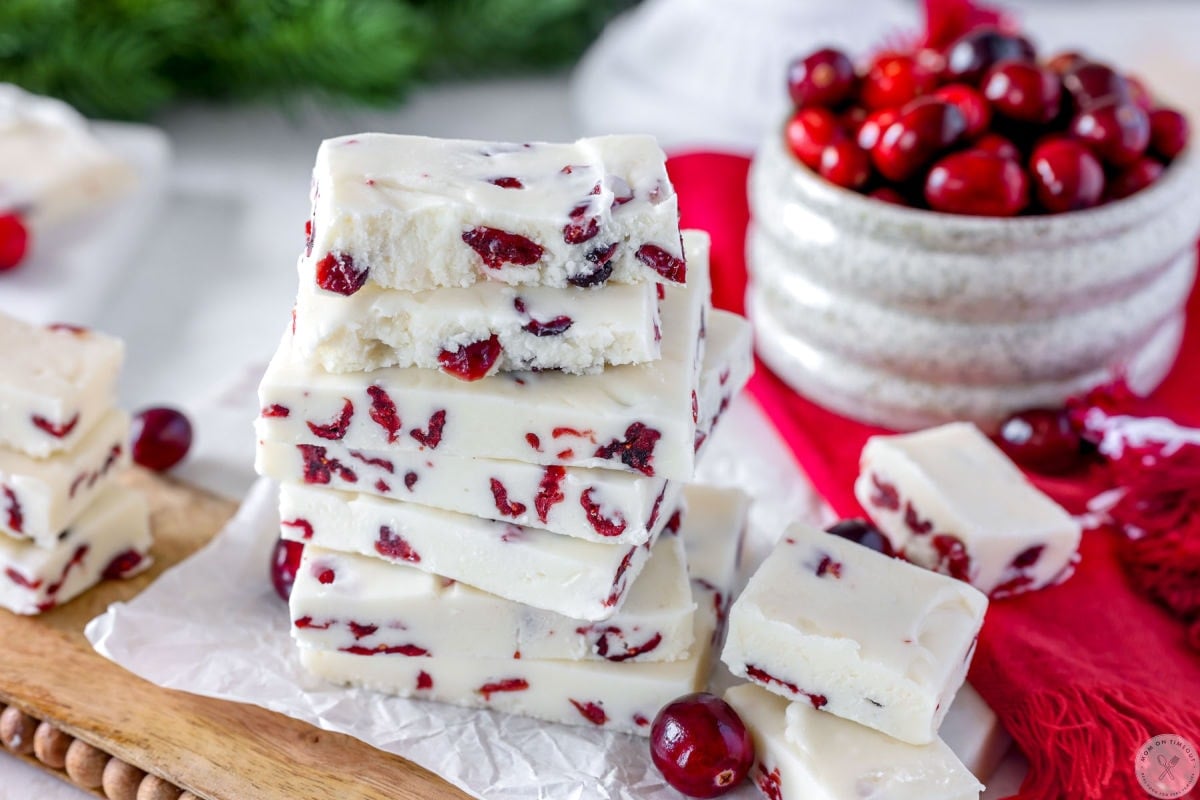 Wide shot of cranberry fudge stacked on marble and wood board. Bowl of cranberries off to the side.