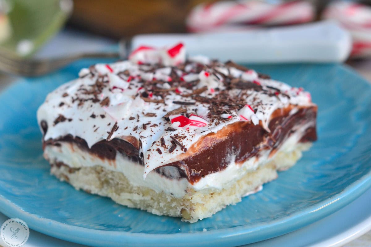 Four layered chocolate peppermint dessert on blue plate. Peppermint lush is topped with crushed candy canes.