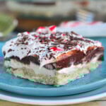 Four layered chocolate peppermint dessert on blue plate. Peppermint lush is topped with crushed candy canes.