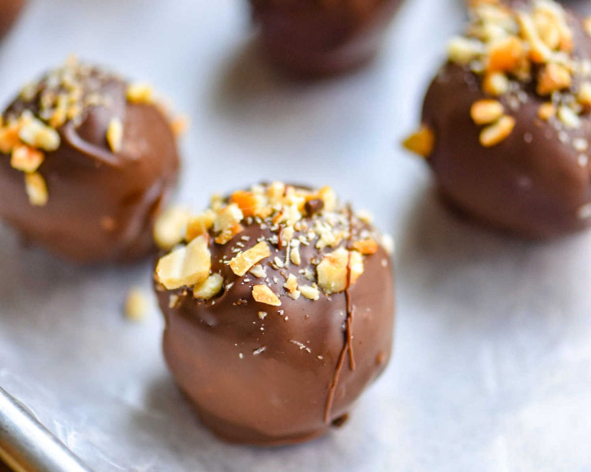peanut butter balls covered in chocolate with crushed peanuts sprinkled on top sitting on a parchment lined baking sheet.