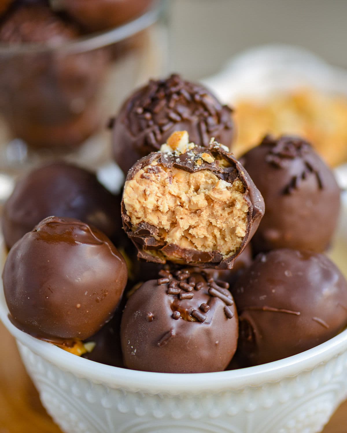 white glass bowl filled with peanut butter balls with rice krispies. each ball is topped with either chocolate jimmies or crushed peanuts.