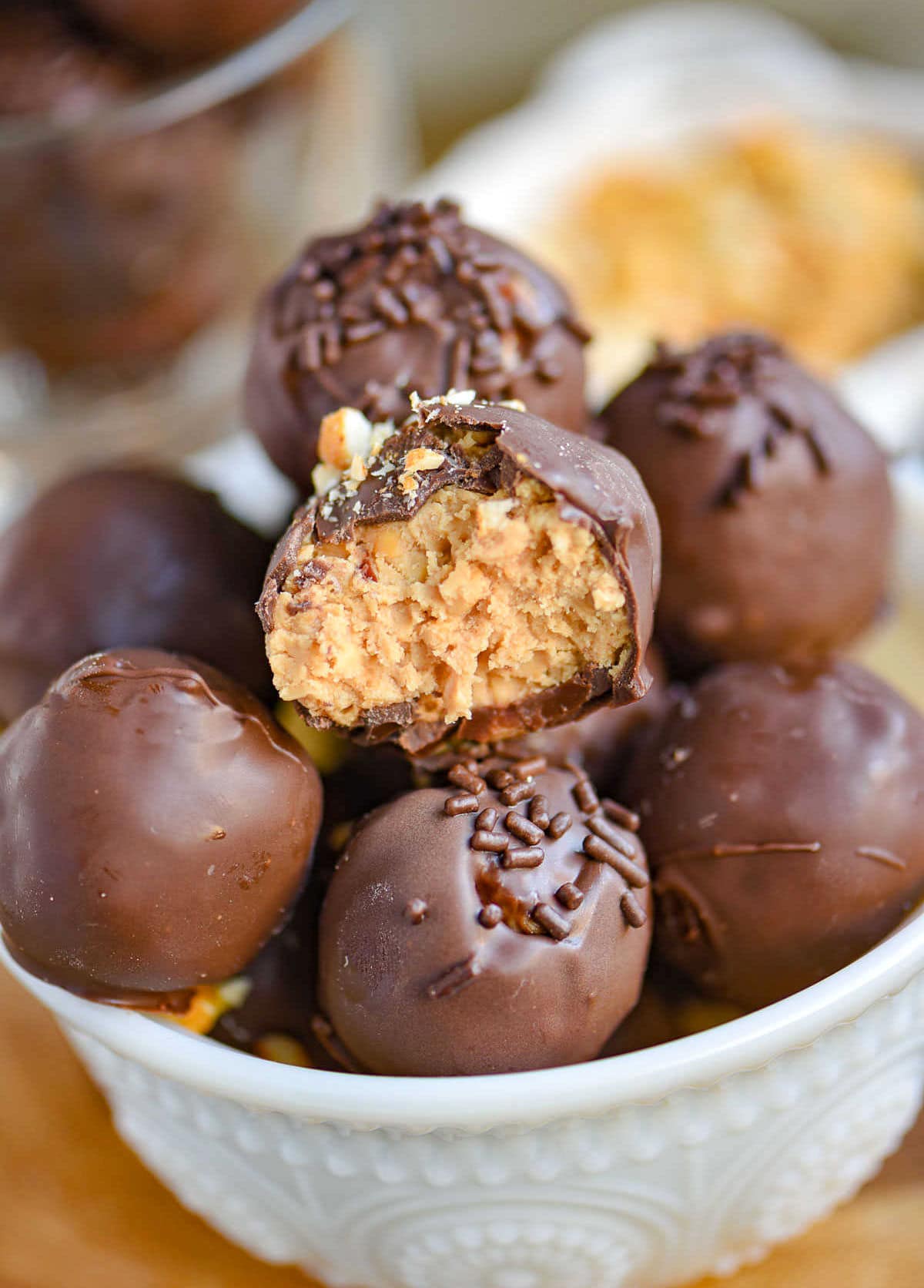 white glass bowl filled with peanut butter balls with rice krispies. each ball is topped with either chocolate jimmies or crushed peanuts.