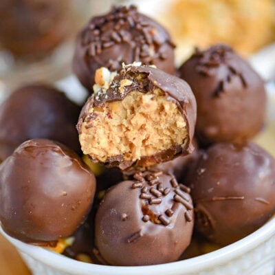 white glass bowl filled with peanut butter balls with rice krispies. each ball is topped with either chocolate jimmies or crushed peanuts.