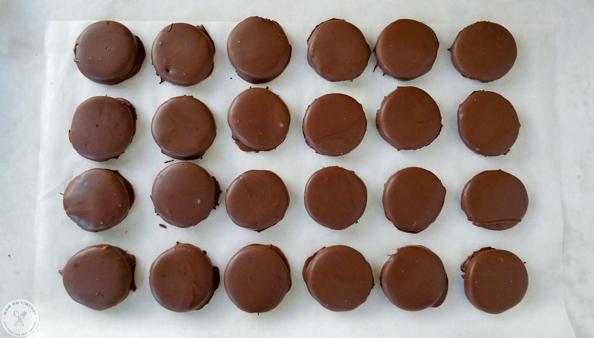Overhead shot of chocolate covered mint patties lined up in a grid on white parchment.