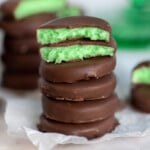 Homemade mint patties stacked five high with the top one split in half. A green cake stand in the background has more patties on it.