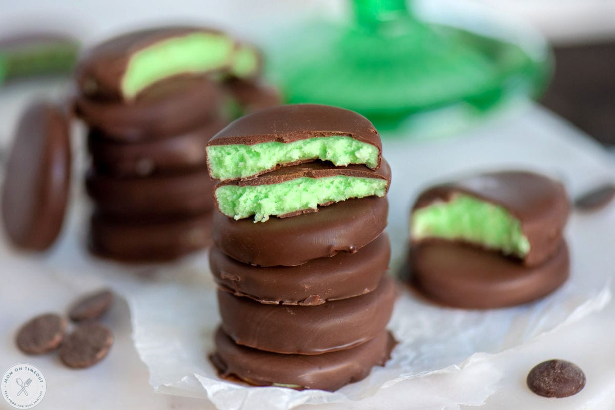Wide shot of chocolate mint patties on a marble board with three of the patties split in half showing the creamy, green mint interior.