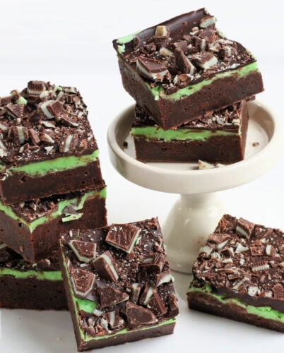 fudge mint brownies stacked on white surface and small white cupcake stand.
