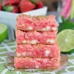 stacked strawberry gooey bars four high on green and white napkin with cut limes and fresh strawberries in background.
