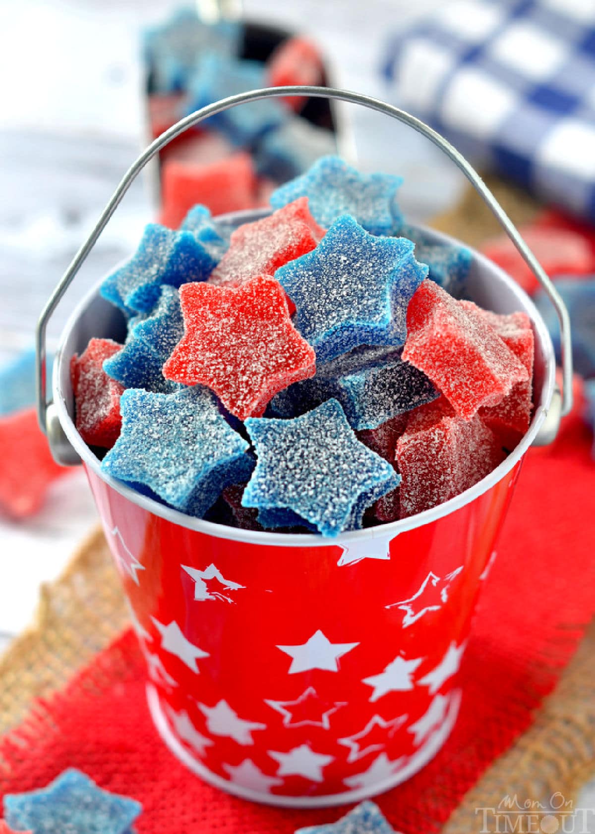Star shaped gumdrops in red and blue are in a red tin bucket. 