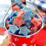 Star shaped gumdrops in red and blue are in a red tin bucket.