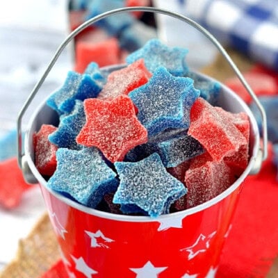Star shaped gumdrops in red and blue are in a red tin bucket.