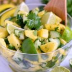 refreshing pineapple cucumber salad in clear plastic bowl with large wood serving spoon.