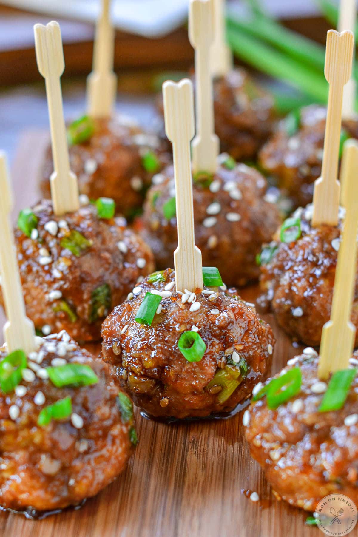 Close up of teriyaki meatballs on cutting board topped with white sesame seed and green onions. 