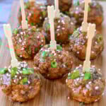 Nine teriyaki meatballs on wood cutting board topped with green onions and sesame seeds. Each meatball has a toothpick in it.