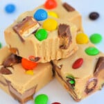 four pieces of peanut butter candy bar fudge stacked on white surface with bite taken out of top piece.