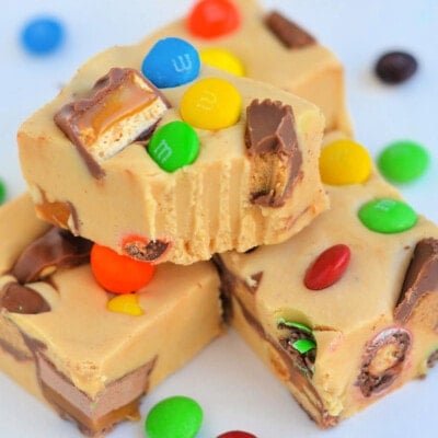 four pieces of peanut butter candy bar fudge stacked on white surface with bite taken out of top piece.