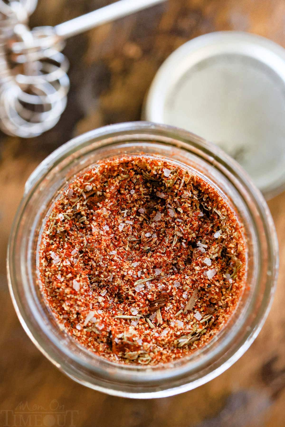 top down look at cajun seasoning in a glass jar with a small whisk to the side of it.