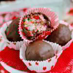 four candies sitting on small cupcake stand with red burlap beneath them. top candy is cut in half to show coconut and cherry interior.