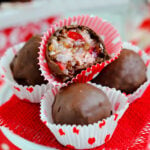 four candies sitting on small cupcake stand with red burlap beneath them. top candy is cut in half to show coconut and cherry interior.