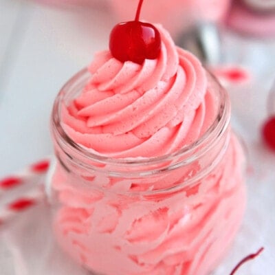 cherry frosting piped into a clear canning jar topped with a maraschino cherry.