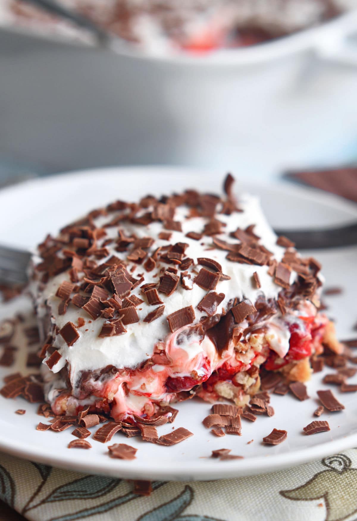 layered dessert made with cherry pie filling and whipped cream. four layers on a white plate topped with chocolate shavings.