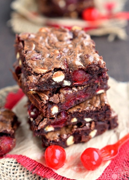 four brownies with cherries stacked on parchment with red burlap underneath and maraschino cherries on the side