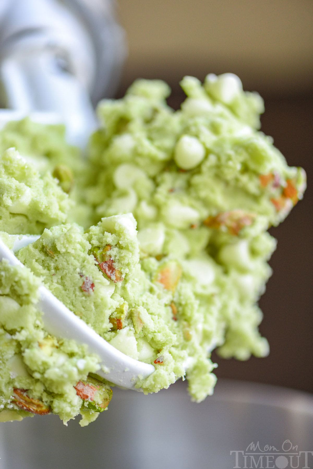 pistachio pudding cookie dough on the beater. pistachios and white chocolate chips can be seen in the dough.