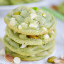 stack of four pistachio pudding cookies on white parchment studded with white chocolate chips and chopped pistachios.