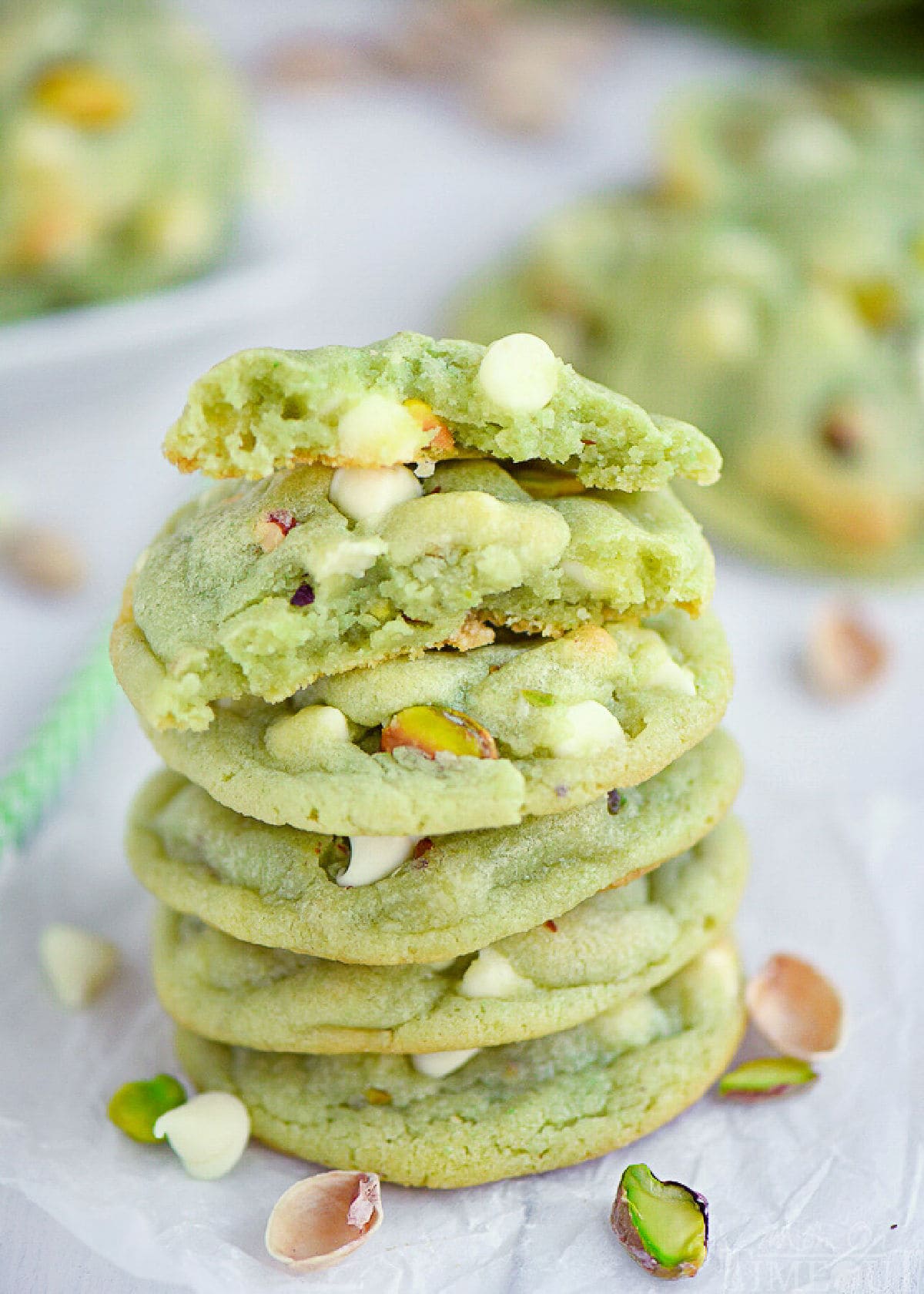 stack of pistachio pudding cookies with the top cookie broken in half. more cookies can be seen in the background.