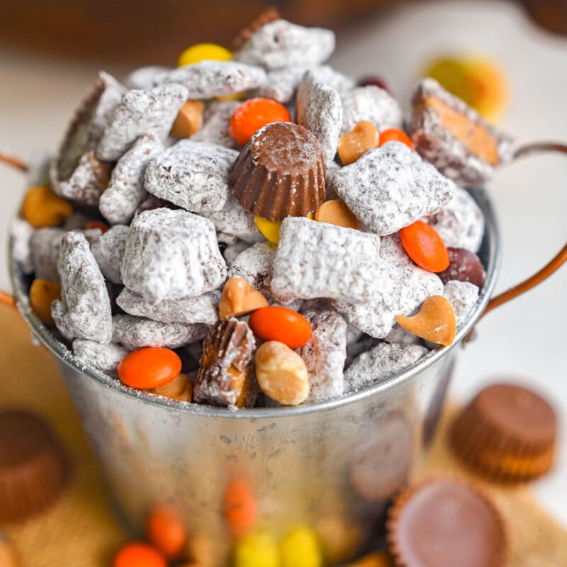 Angled overhead shot of a small metal bucket filled with muddy buddies with Reese's pieces and miniatures.