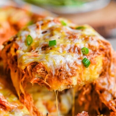 loaded mashed potato casserole topped with pulled pork and cheese. a serving spoon has scooped a large serving out of the casserole dish.