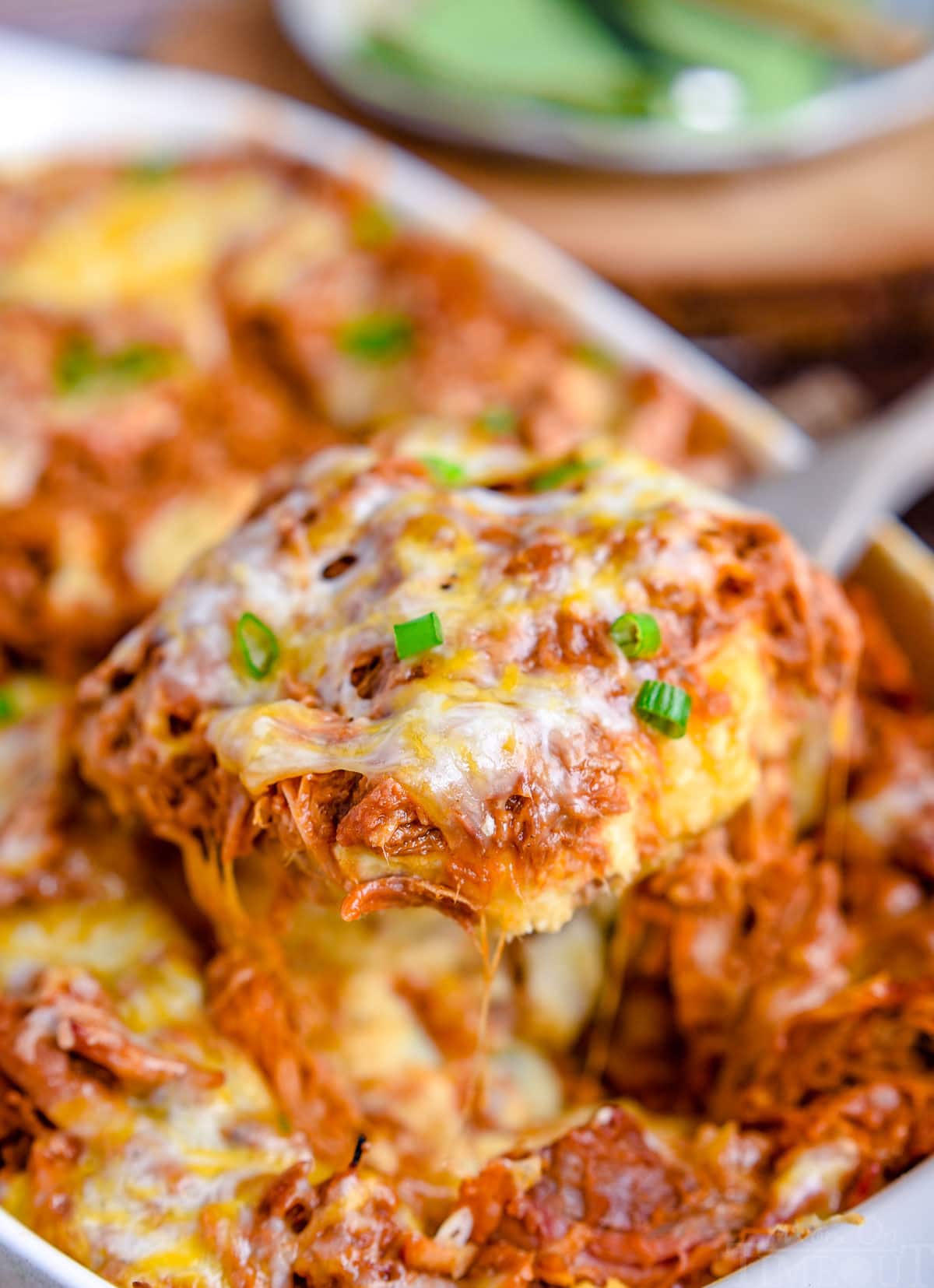 large scoop of loaded mashed potato casserole with pulled pork on top being lifted out of the casserole dish.