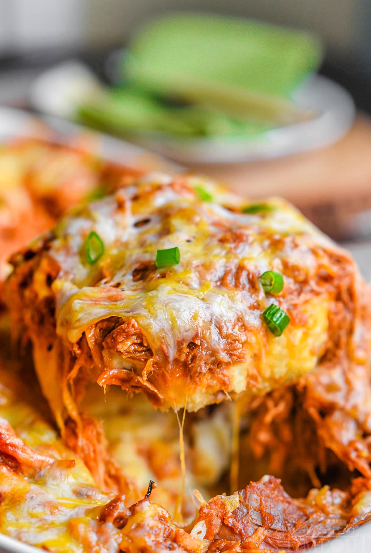 loaded mashed potato casserole topped with pulled pork and cheese. a serving spoon has scooped a large serving out of the casserole dish. 