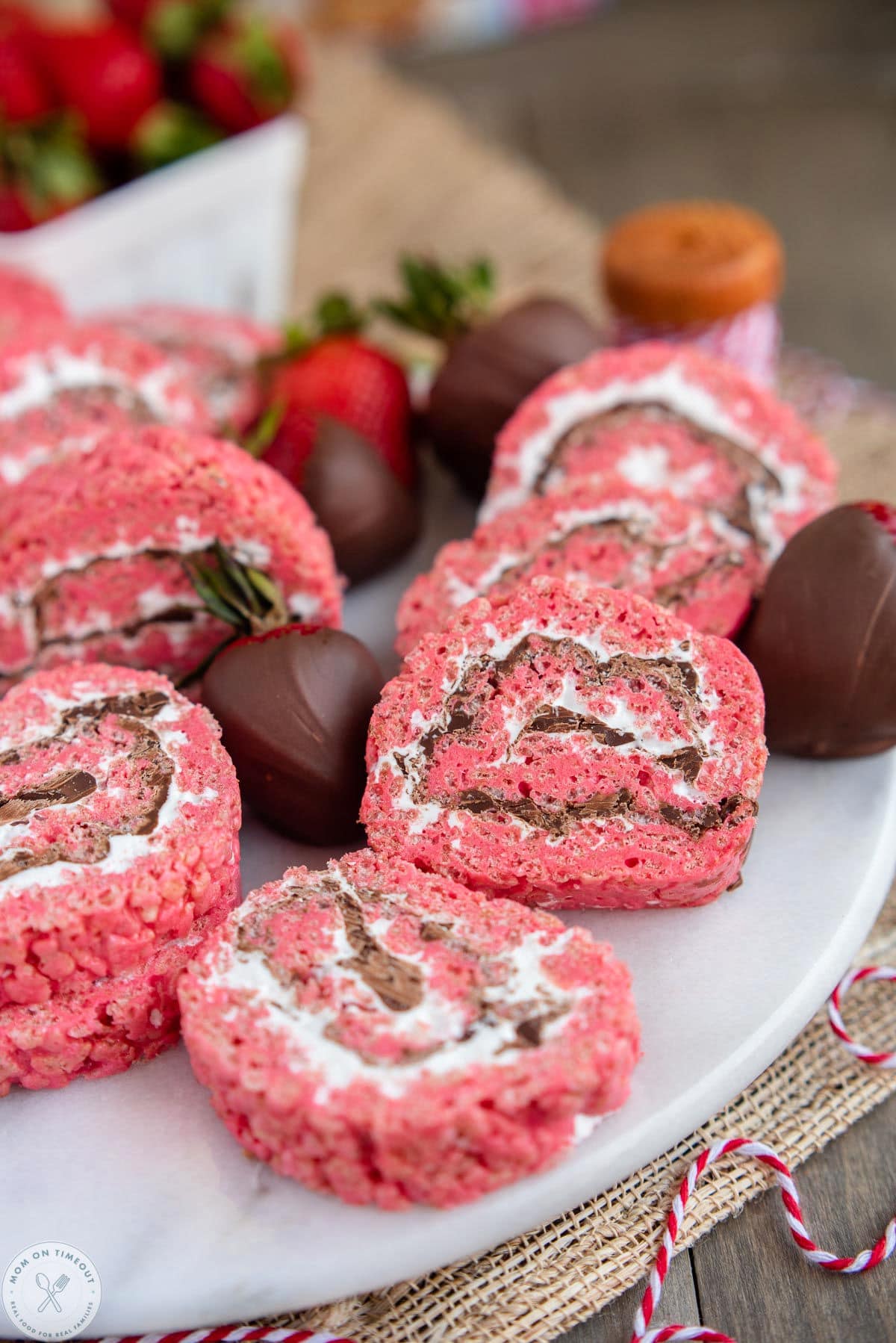 Chocolate covered strawberry rice krispie treat pinwheels on a white serving tray next to chocolate covered strawberries.